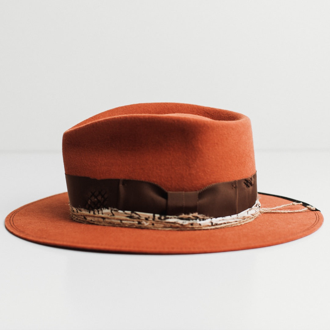 Left side view of the Marrakech spiced pumpkin felt hat by PHYLLi Designs with triple twine wraps and black and white sari silk trim.