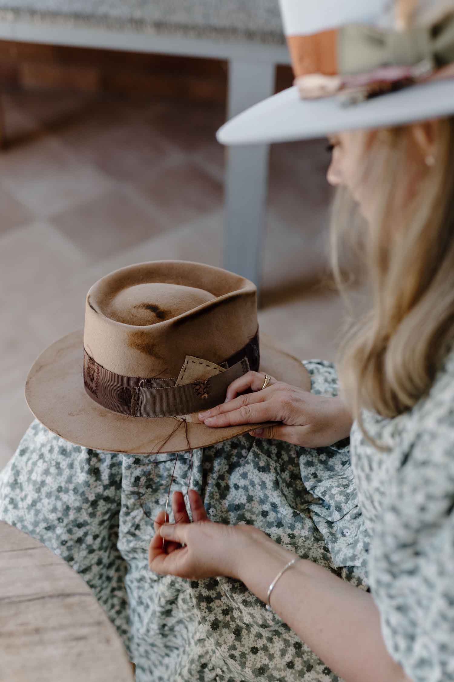 Founder of PHYLLi Designs hand-stitching a patch detail onto a distressed custom hat band.