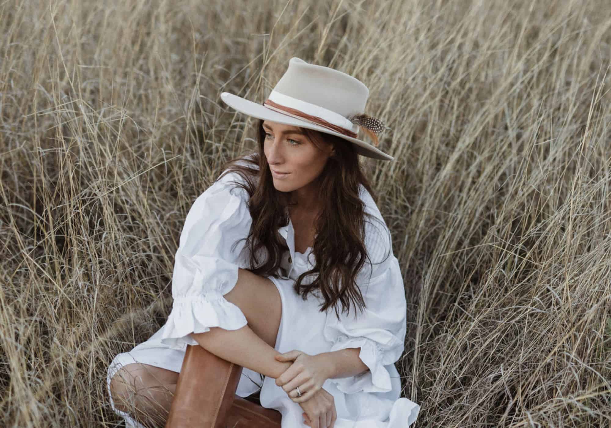 Grace Quast wearing Dartbrook felt hat by PHYLLi Designs sitting in golden grass at Domang NSW