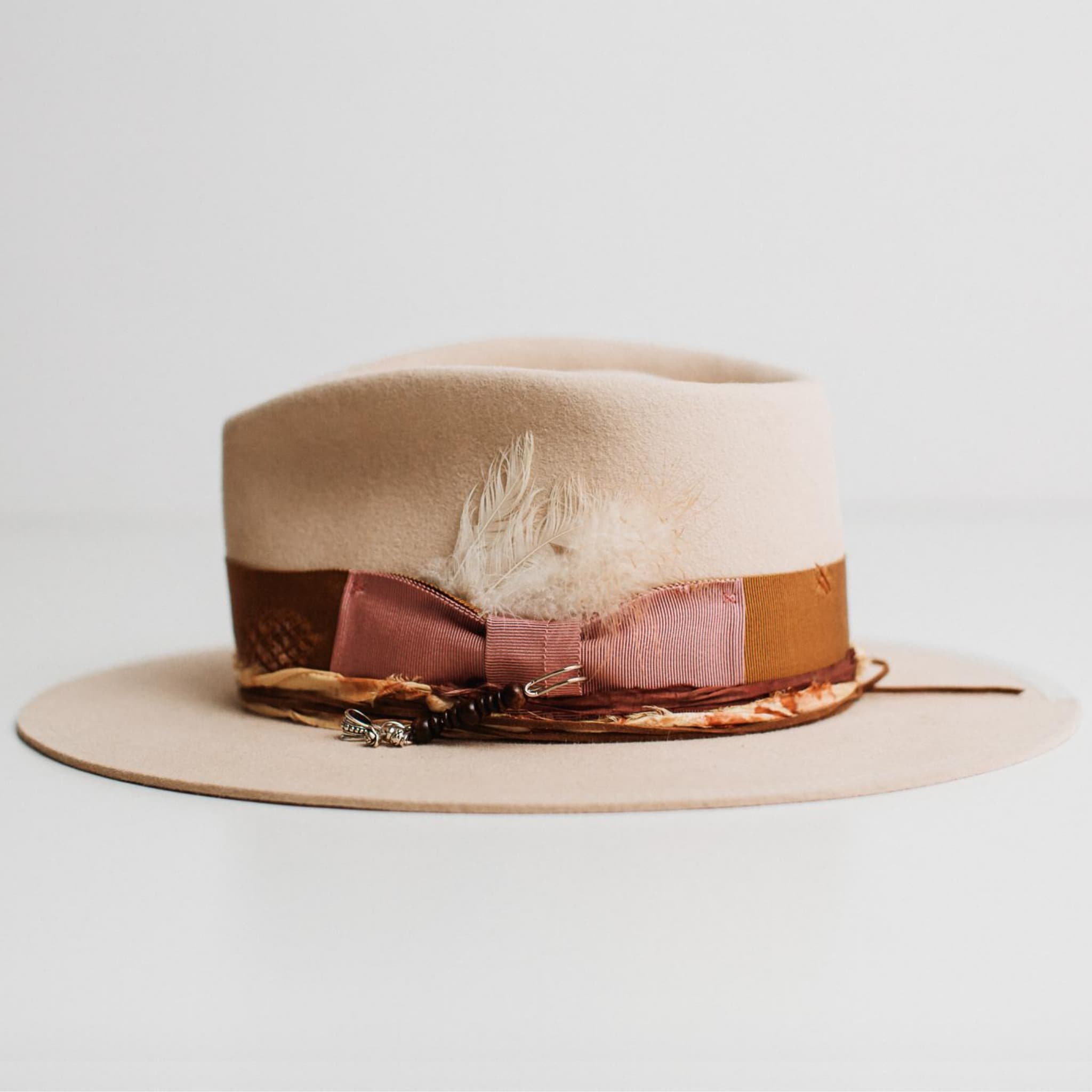 Left side view of Malibu beige felt hat by PHYLLi Designs showing copper band and silver hat pin.