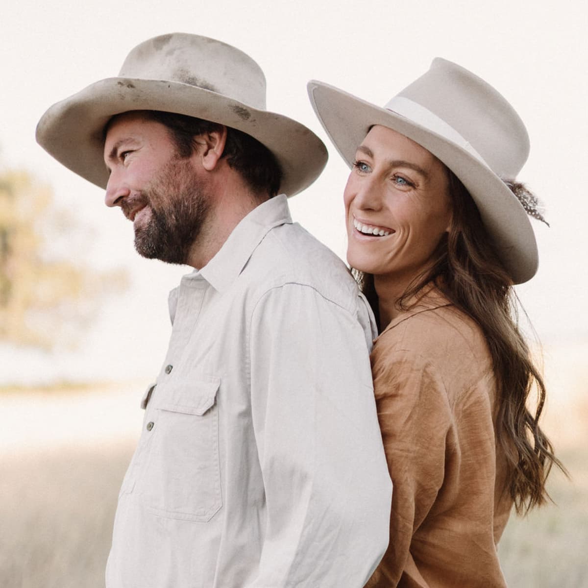 Grace Quast and husband wearing wide-brimmed hats standing back-to-back with a blurred natural background