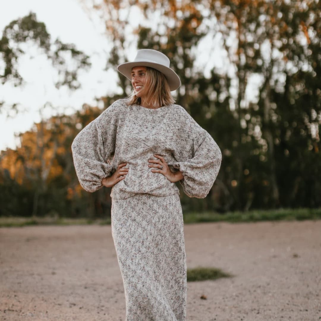 Grace Brennan in a knitted dress and hat standing outdoors with trees in the background