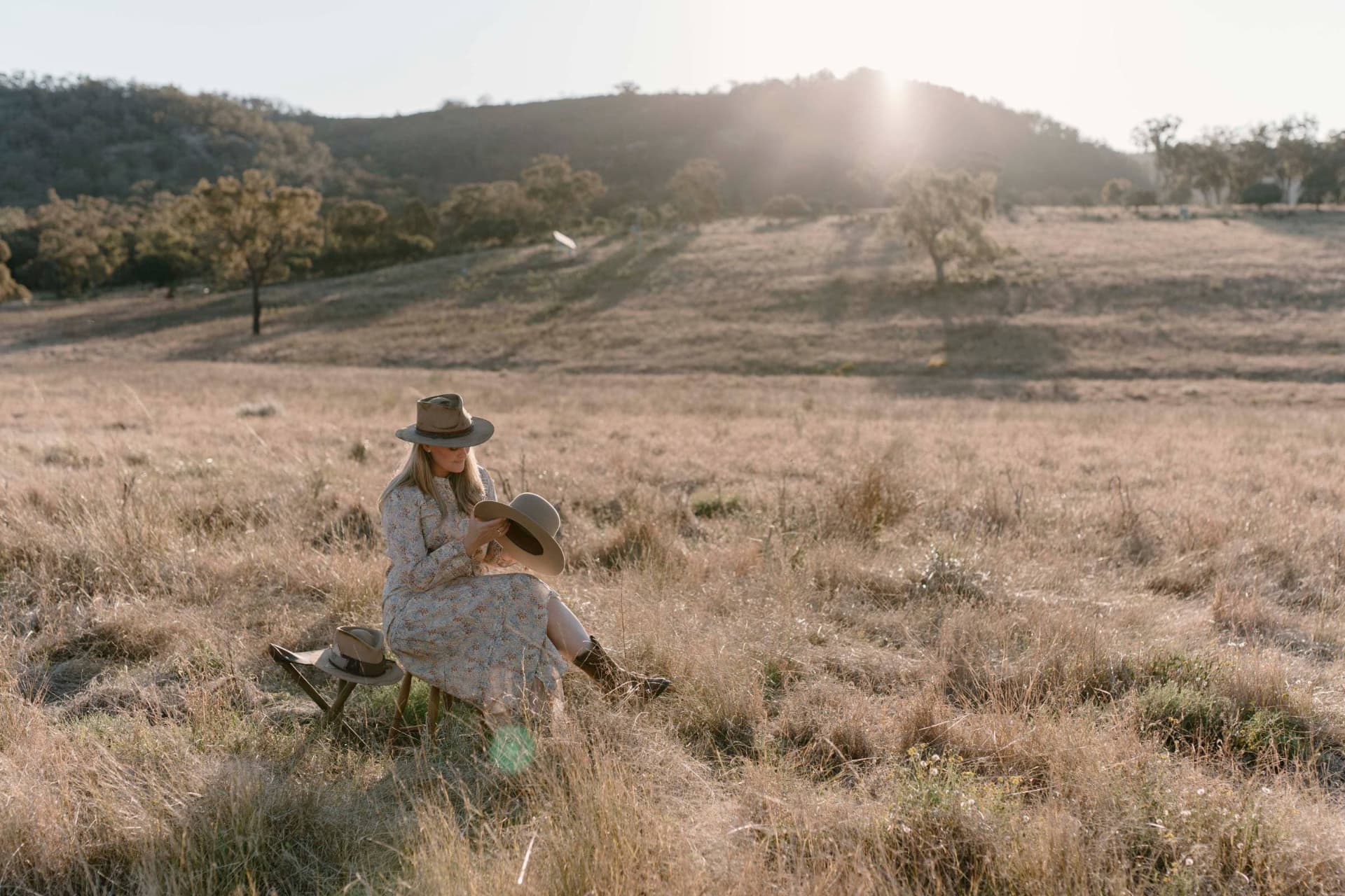 Laura Hall sitting in a field stitching one of her handcrafted custom hats made in regional Australia