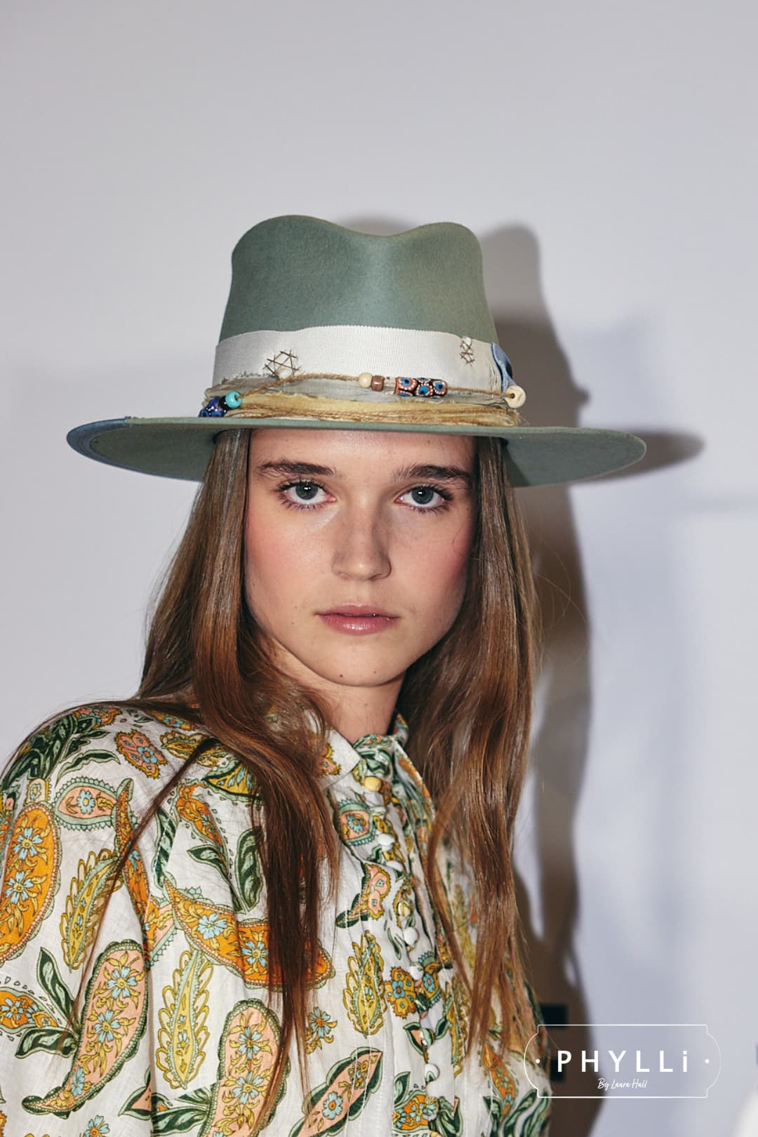 Close up woman wearing the Accra sage felt hat by PHYLLi Designs with ivory Japanese grosgrain ribbon band and cornflower bow in studio portrait setting.