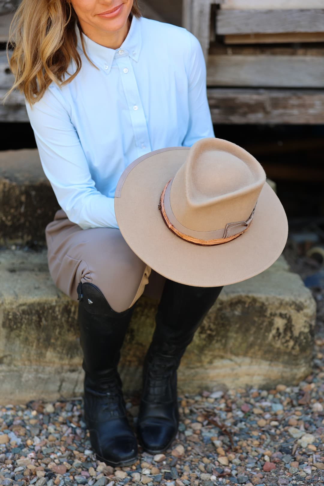 Woman holding the Alexander Camel felt hat by PHYLLi Designs with copper sari silk trim while seated outdoors in riding attire.