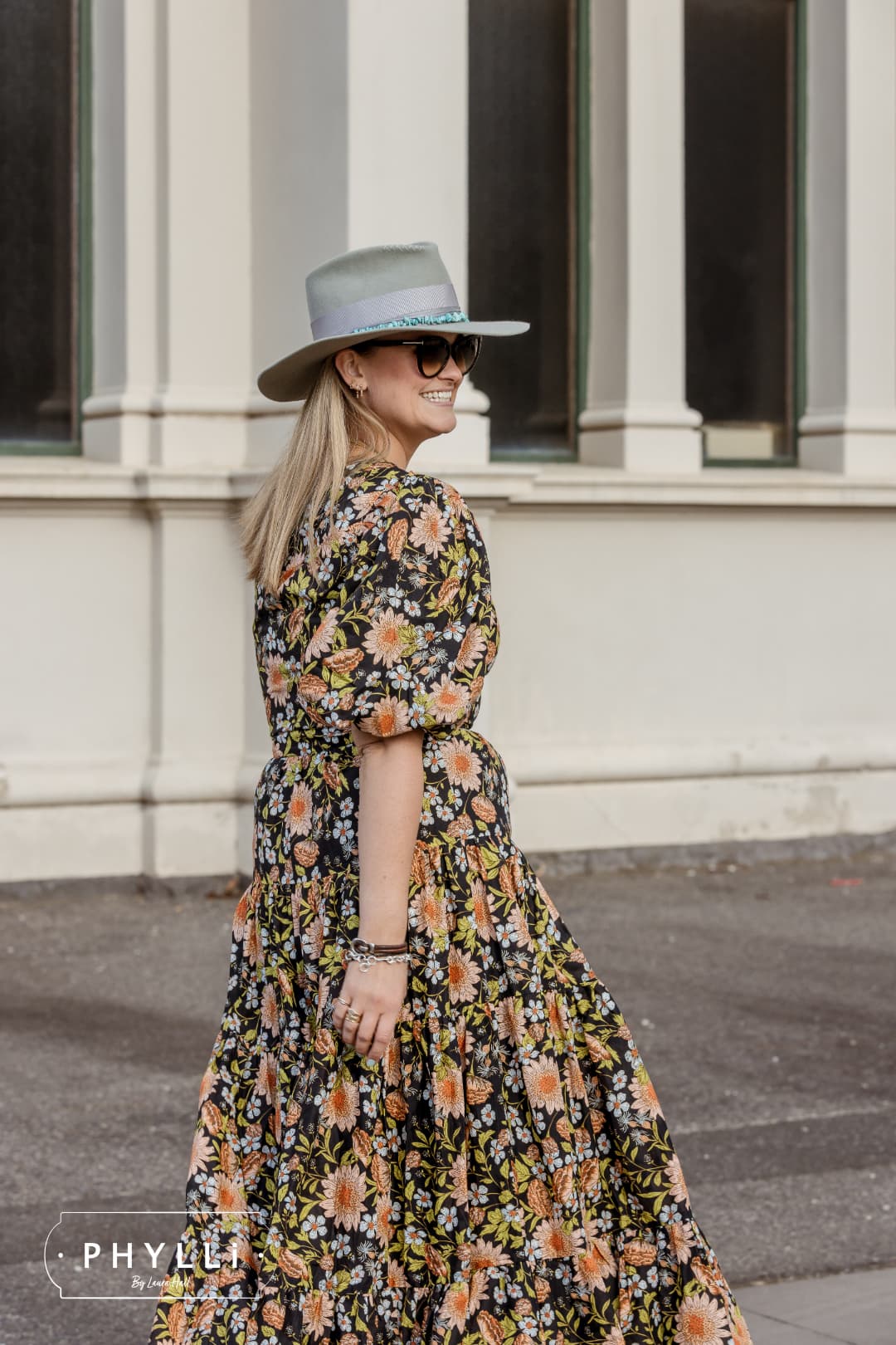 PHYLLi founder and designer Laura Hall wearing the Aurora sage felt hat by PHYLLi Designs with turquoise hat necklace and dove grosgrain bow band outside heritage building columns.