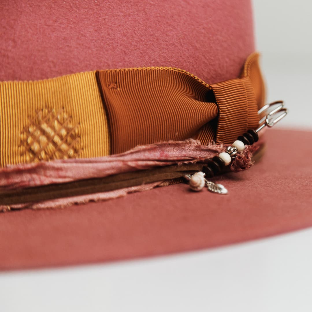 Close up detail of the Barbados Rose felt hat showing rust grosgrain bow and silver hat pin with wooden beads, pendant charm and shell.