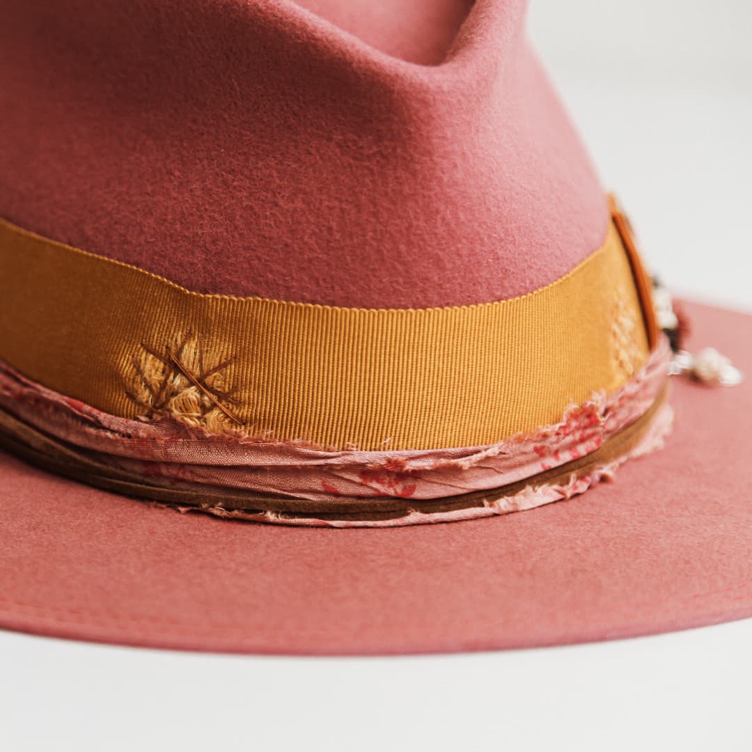 Close up detail of the Barbados Rose felt hat showing distressed turmeric grosgrain band with copper darned patch and candy and rose sari silk trimming.
