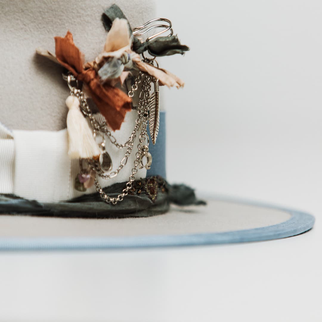 Detail of Bleu de France felt hat showing silver chunky hat pin with ivory tassel, sari silks and silver chain charms.