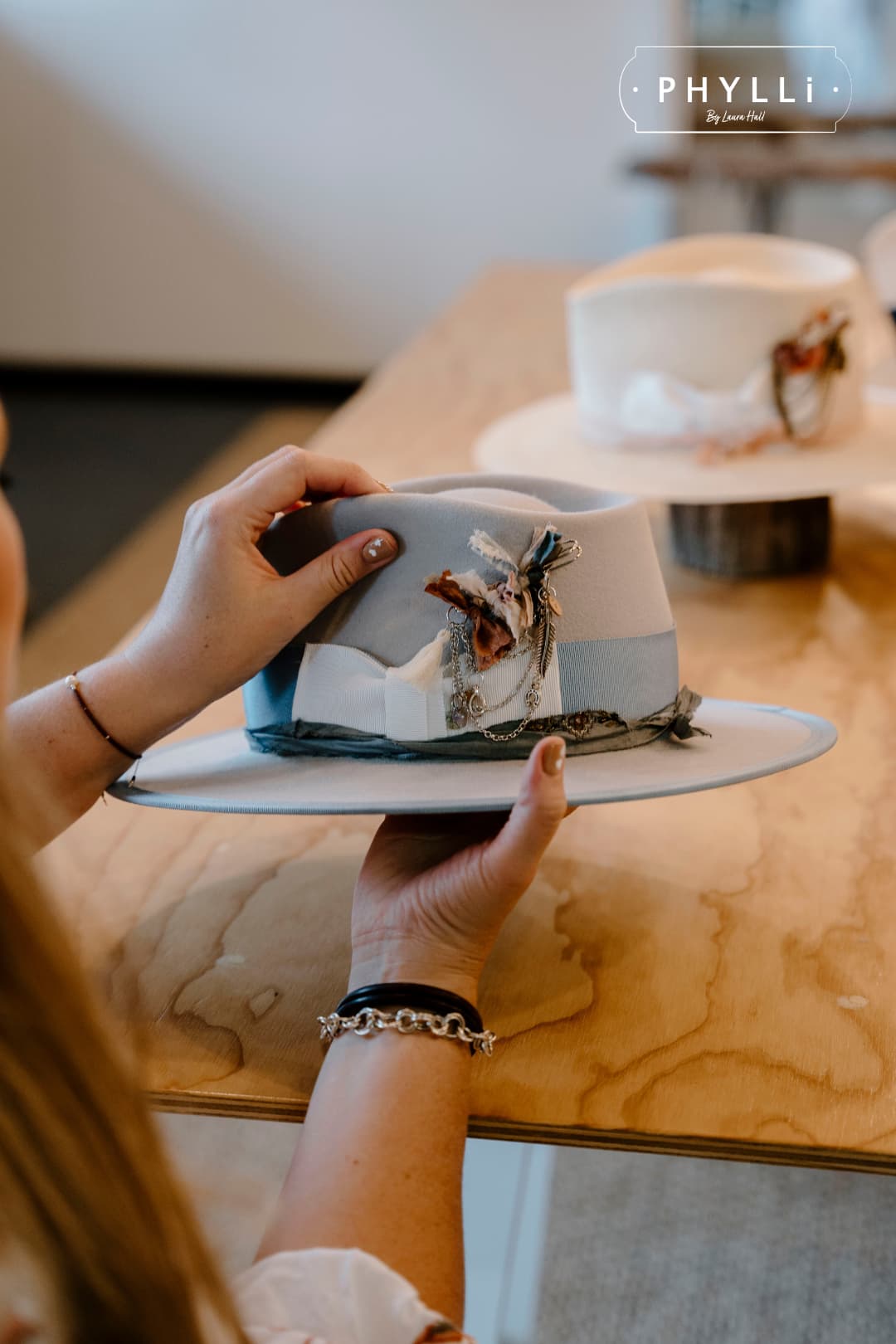 Hands holding Bleu de France felt hat in Dove with Cornflower grosgrain band, Ivory bow and Smokey Blue sari silk trim in the PHYLLi studio.