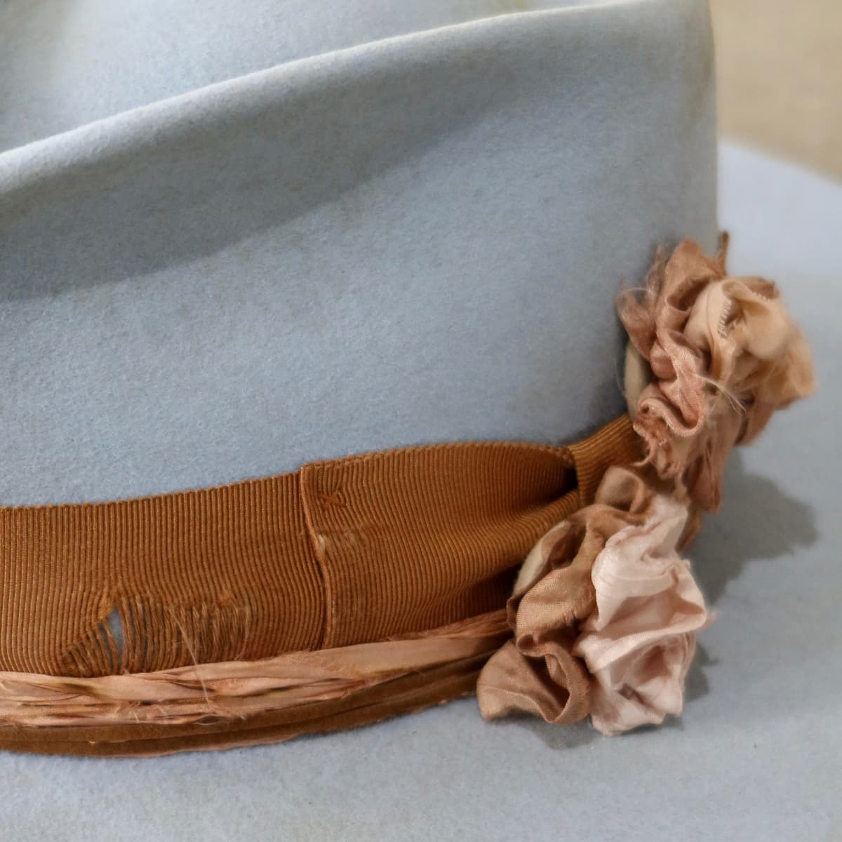 Close up detail of the Blue Bloom felt hat showing Dirty Rose sari silk Lapel Bloom and distressed copper grosgrain band.