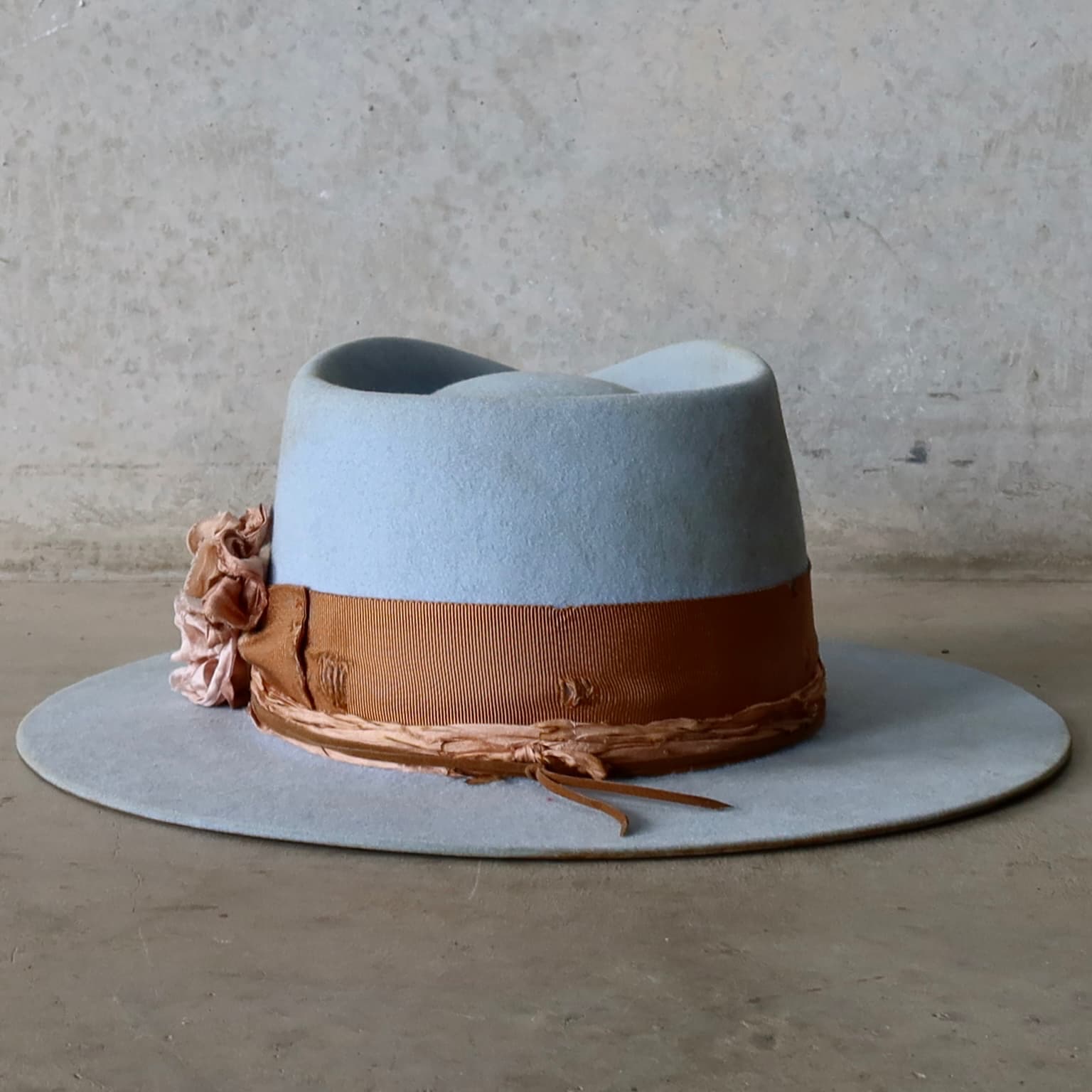 Back view of the crystal blue felt hat Blue Bloom by PHYLLi Designs featuring distressed copper grosgrain band and tan suede string wrap.