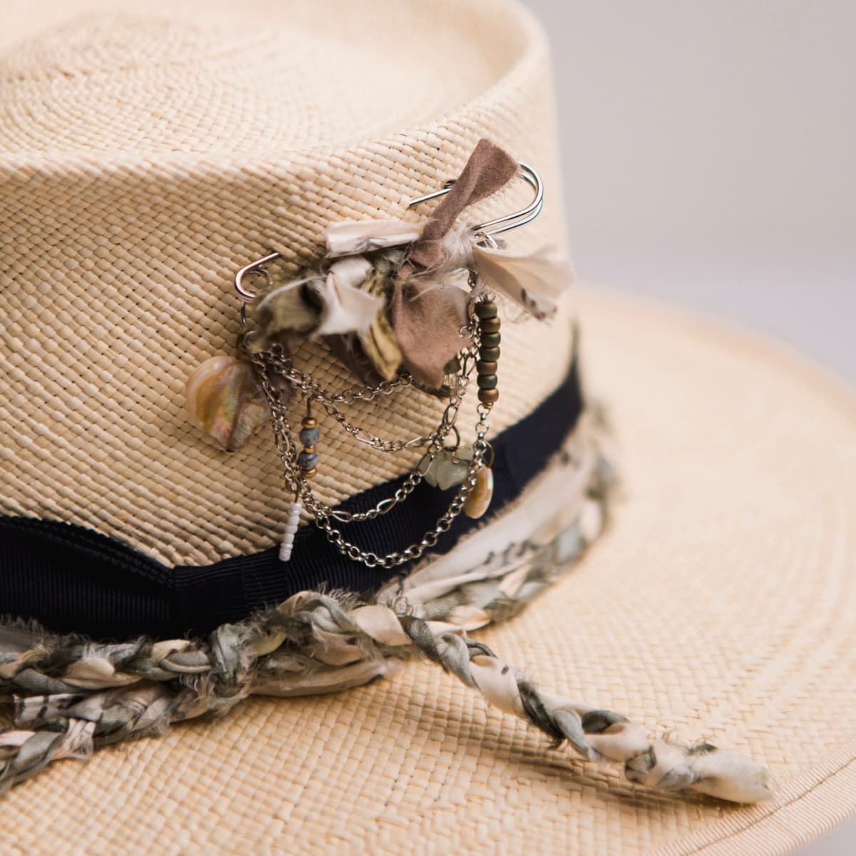 Close up detail of the Blue Jean Panama hat showing silver chunky hat pin with sari silks, charms and pearl.