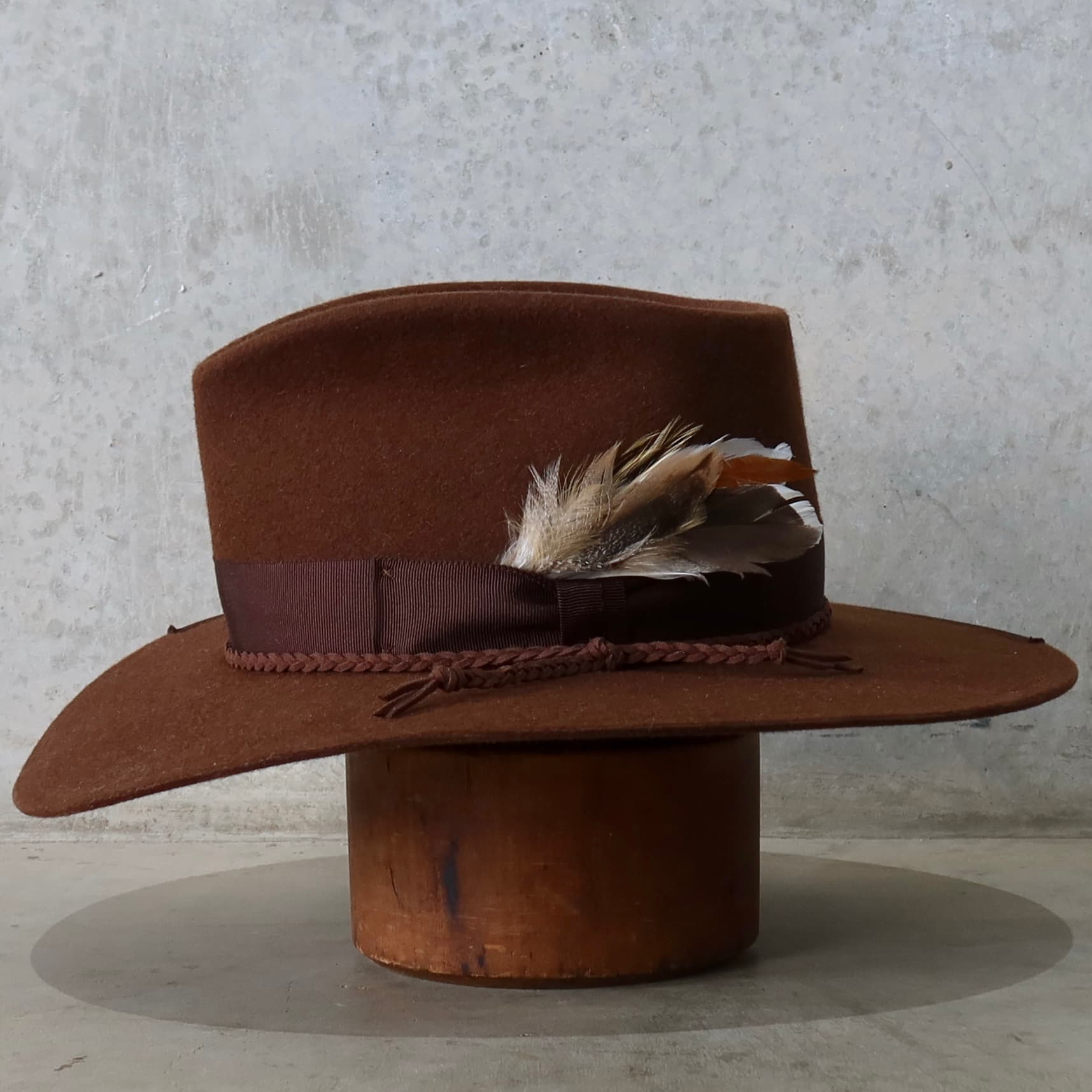 Left side view of the chocolate felt hat Botero by PHYLLi Designs with dark brown Japanese grosgrain band and feather trim.