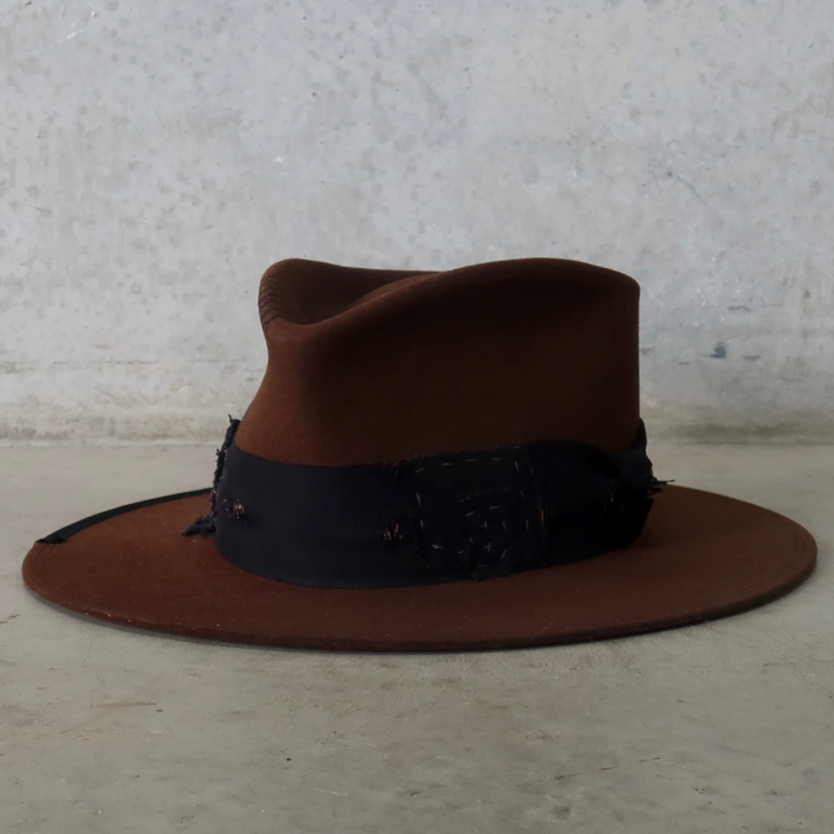Front left angle of the chocolate felt hat Brenner Limited Edition by PHYLLi Designs with distressed black grosgrain bow band and patchwork trims.