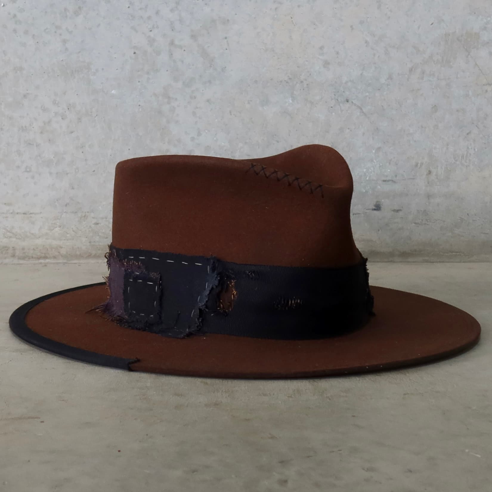 Front right angle of the chocolate felt hat Brenner Limited Edition by PHYLLi Designs featuring black hand-stitched cross detailing.