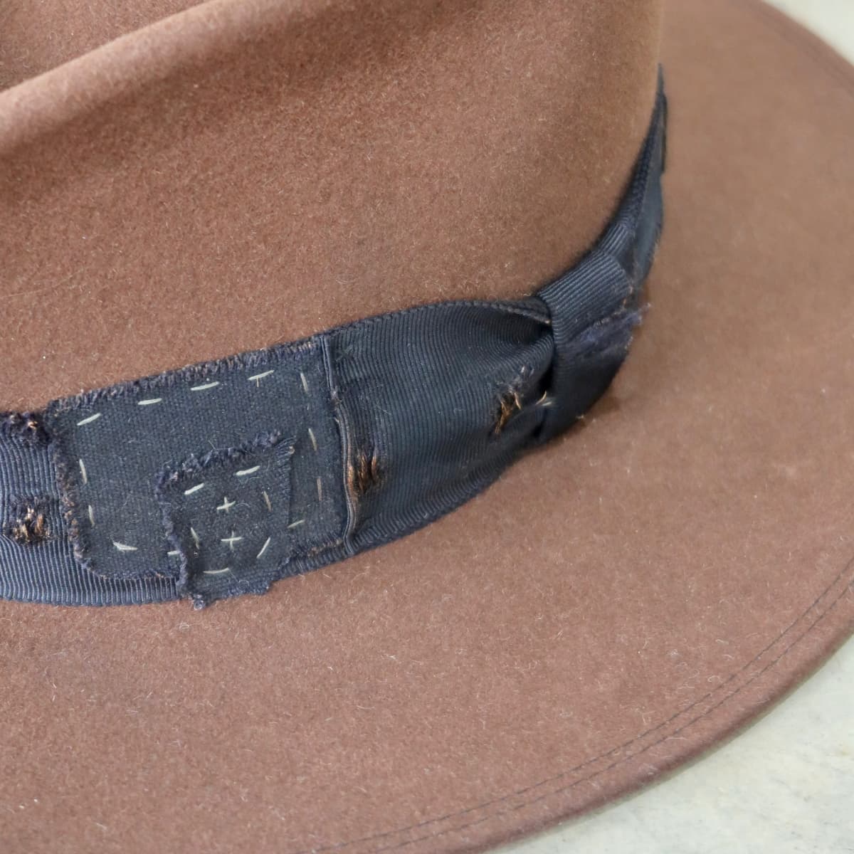 Close up detail of the Brenner Limited Edition felt hat showing distressed black grosgrain trim and worn fabric patch.