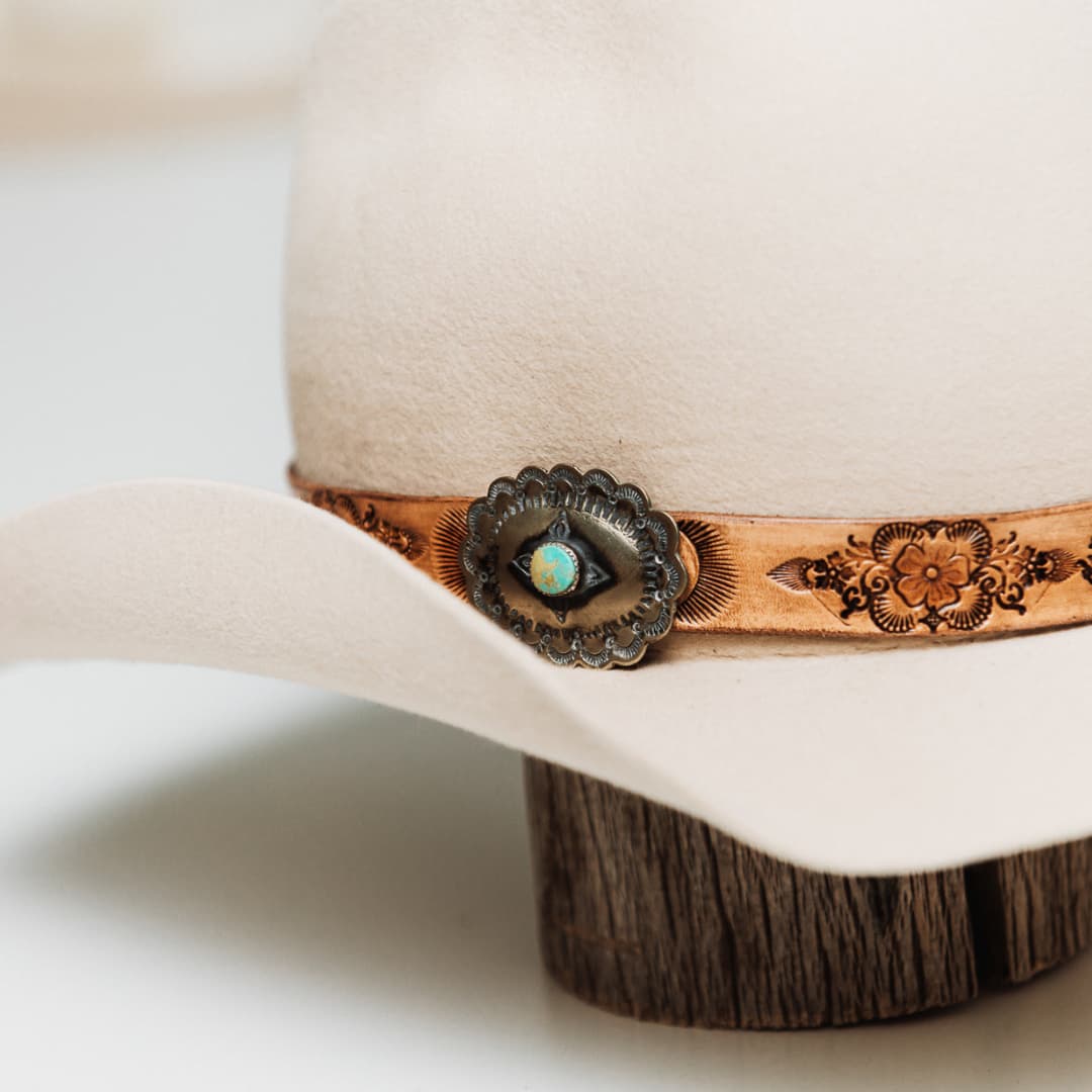Close up detail of the PHYLLi x Buffalo Girl Palamino Mandala Hat Band with Navajo Concho showing genuine vintage Navajo concho with Nevada turquoise set on hand tooled Mandala leather hat band on a beige felt cowboy hat by PHYLLi Designs.