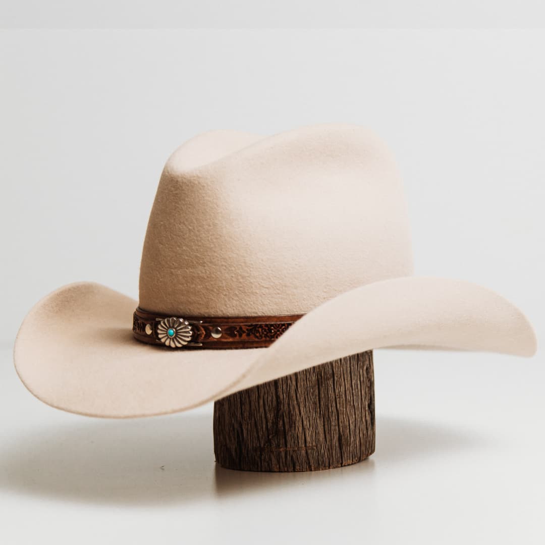 Front left angle of the Phylli x Buffalo Girl Rugged Desert Hat Band Western Floral with antique brown hand tooled leather hat band and Western Floral turquoise conchos on a beige felt cowboy hat by PHYLLi Designs.