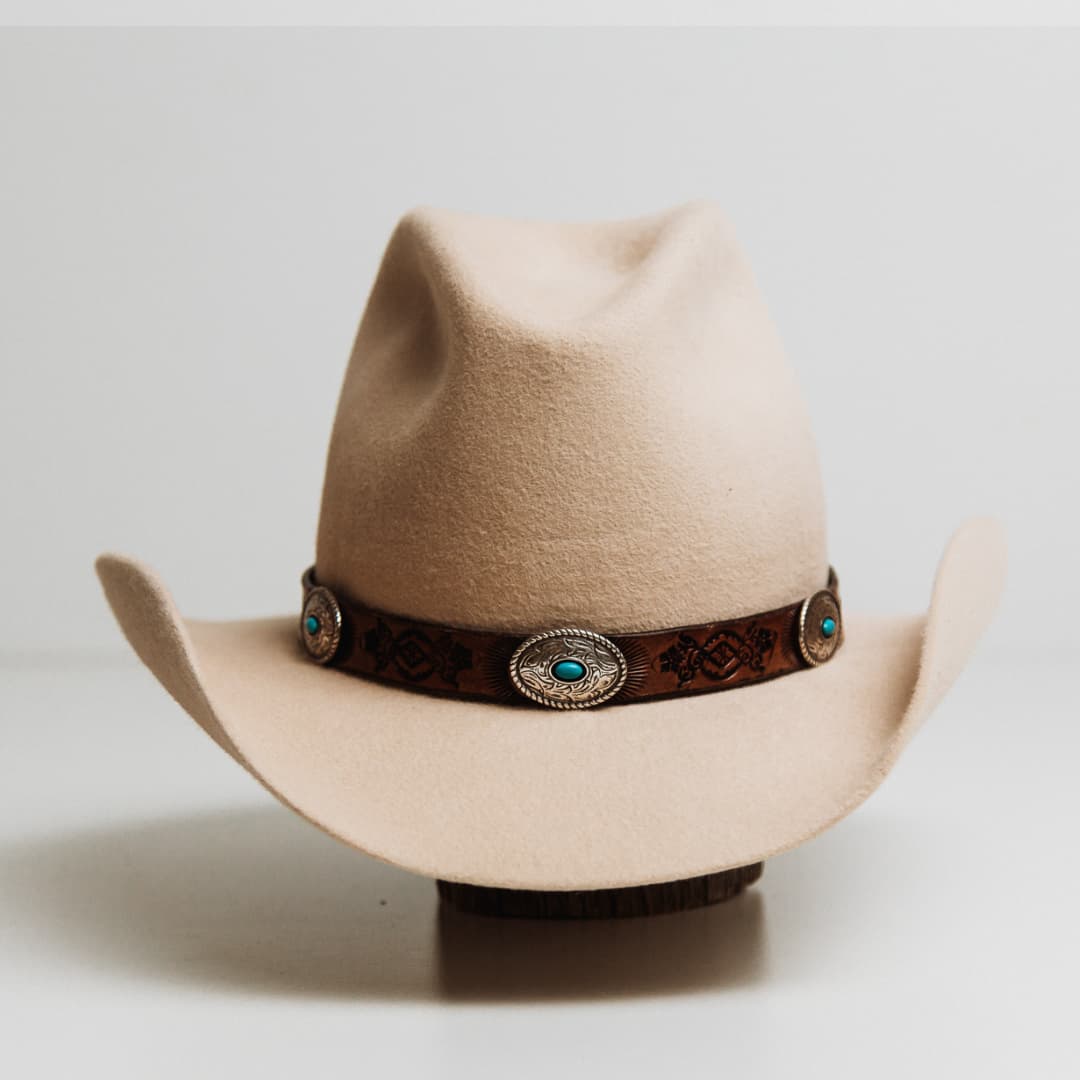 PHYLLi x Buffalo Girl Rugged Desert Tie Back Hat Band with antique brown hand tooled leather hat band featuring five turquoise conchos on a beige felt cowboy hat by PHYLLi Designs. 