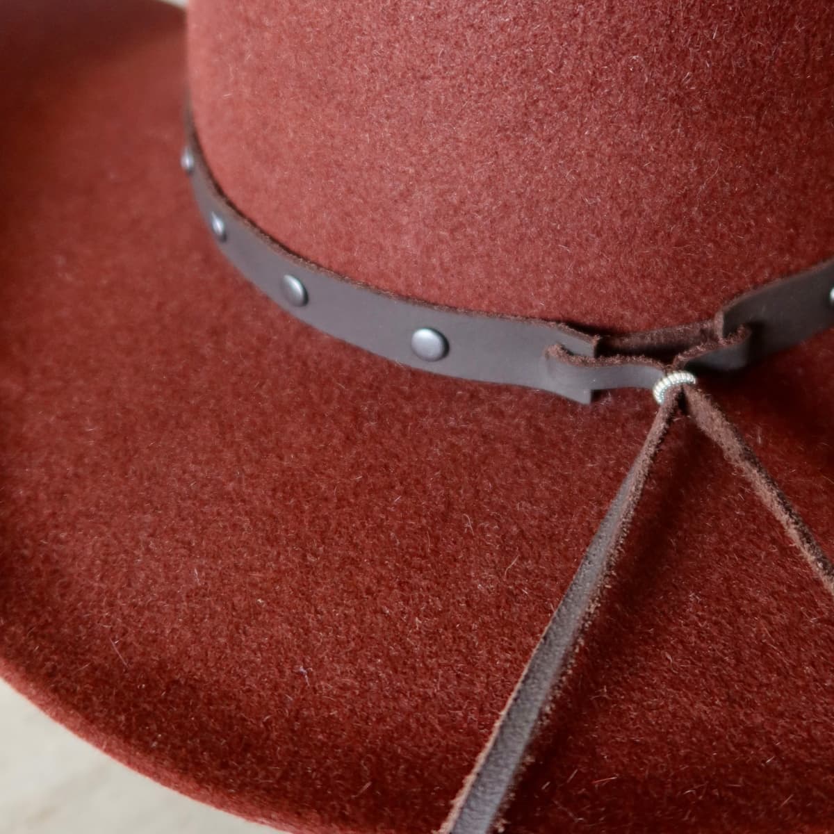 Close up detail of the Burgundy felt cowboy hat showing dark brown leather tie back closure.