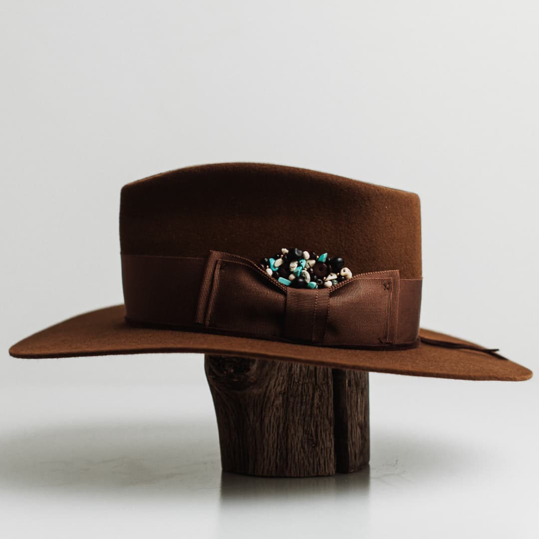 Left side of the Calaveras caramel felt hat by PHYLLi Designs with chocolate grosgrain double bow band and skull bead cluster.