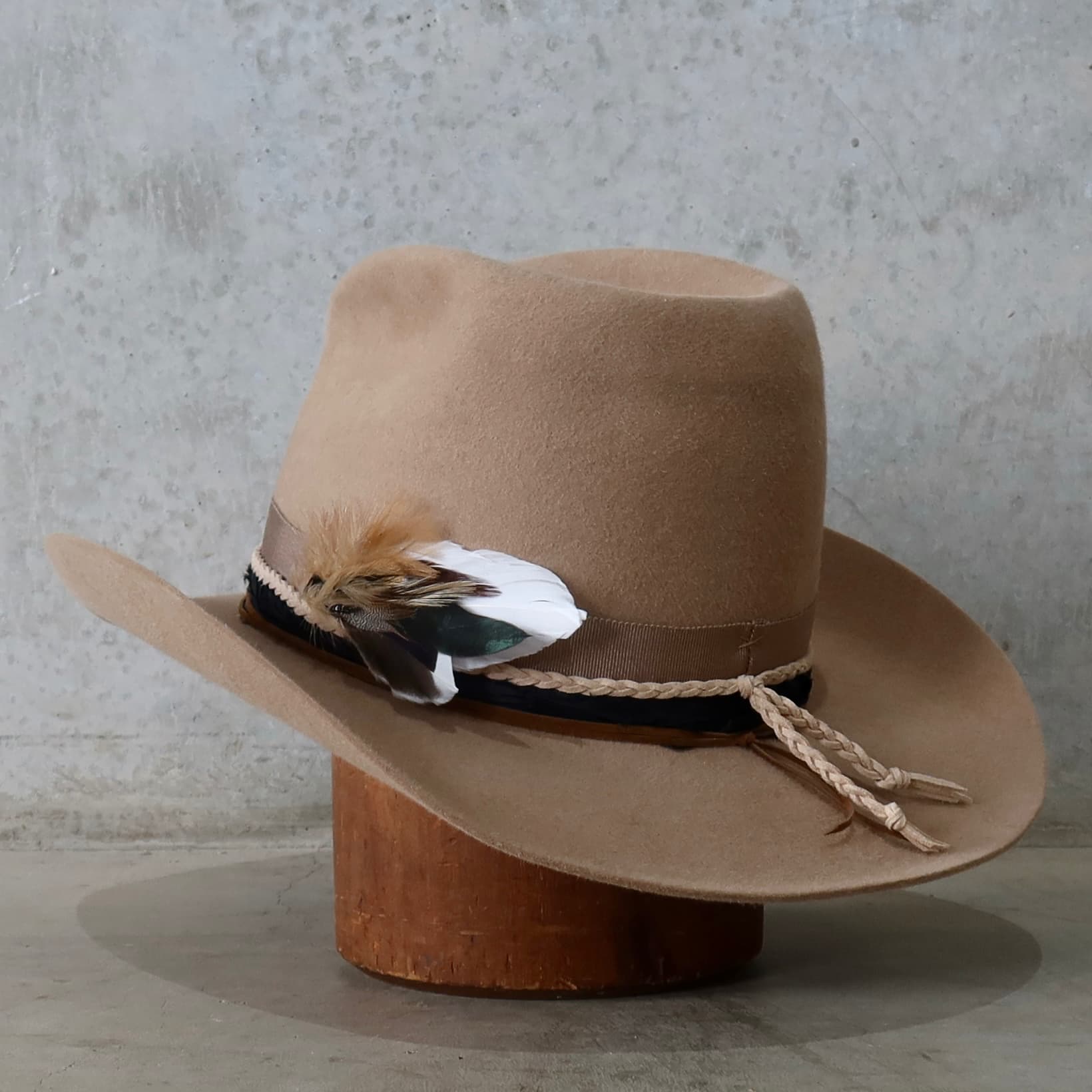 Back left angle of the camel felt cowboy hat Casey by PHYLLi Designs with taupe grosgrain band and fallen feather bunch.