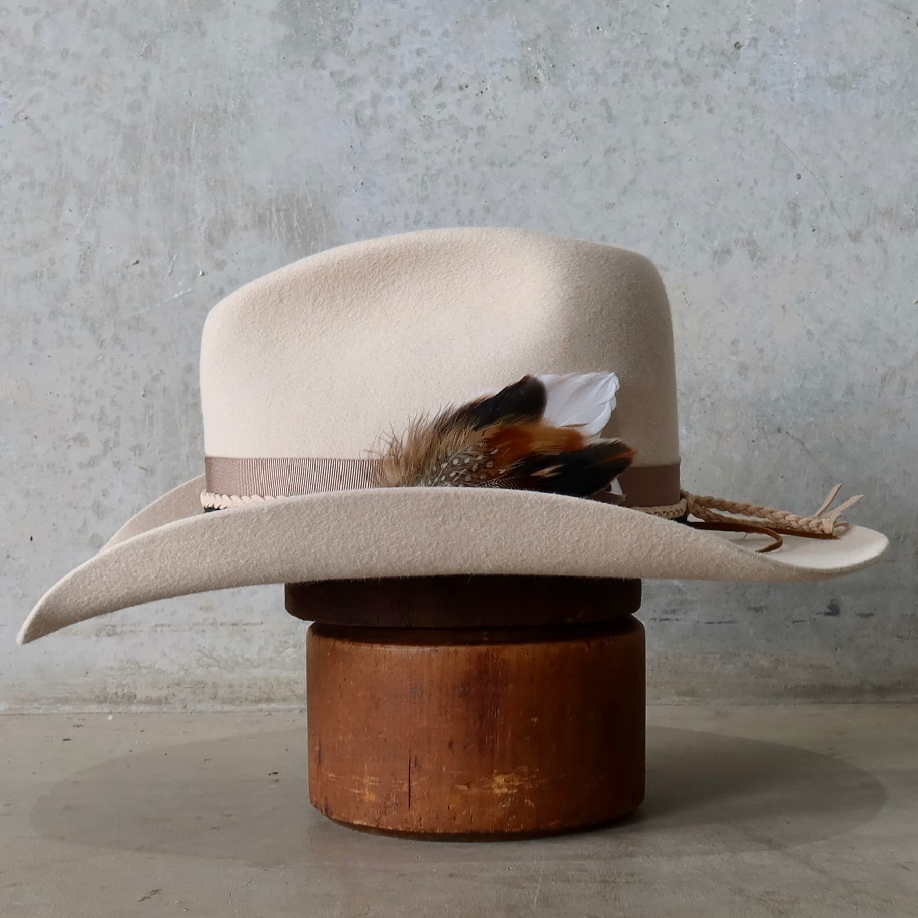 Left side view of the beige felt cowboy hat Casey Beige by PHYLLi Designs with taupe grosgrain band, black sari silk trimming and feather detail.