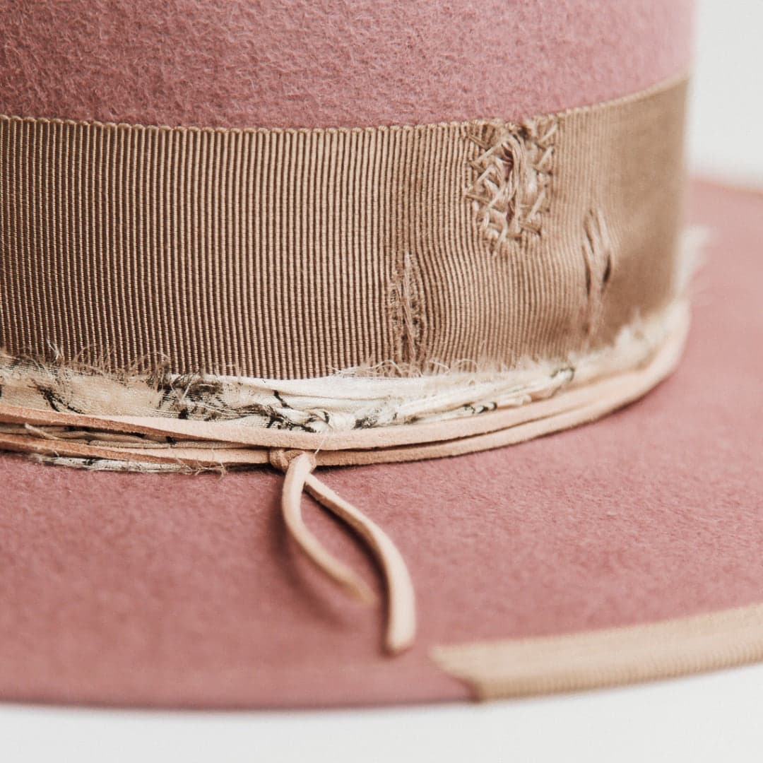 Close up detail of the Celia blush felt hat by PHYLLi Designs showing distressed taupe grosgrain band with patched darning and black and white sari silk trim.