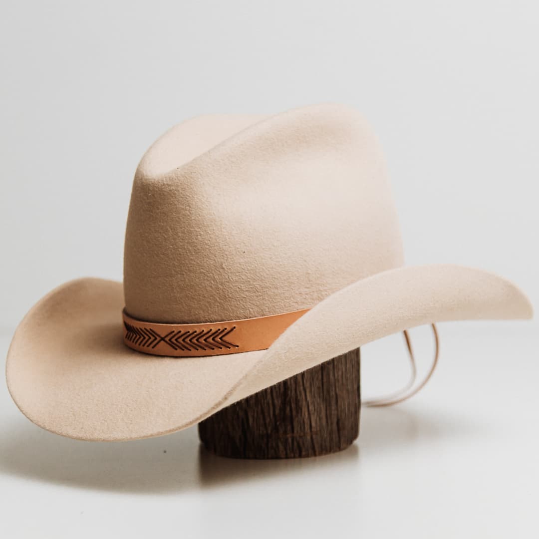 Front left angle of the Chevron Hat Band featuring Palomino cow hide band with chocolate waxed cord chevron pattern on a beige felt cowboy hat by PHYLLi Designs.