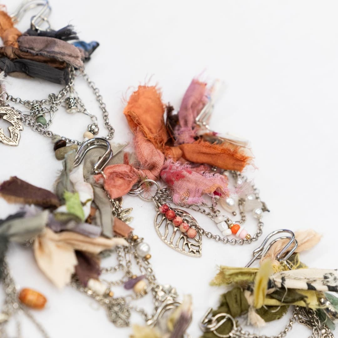 Close up detail of chunky hat pins showing layered sari silk ribbons in coral, pink and green with silver chains, bead charms and leaf pendants.