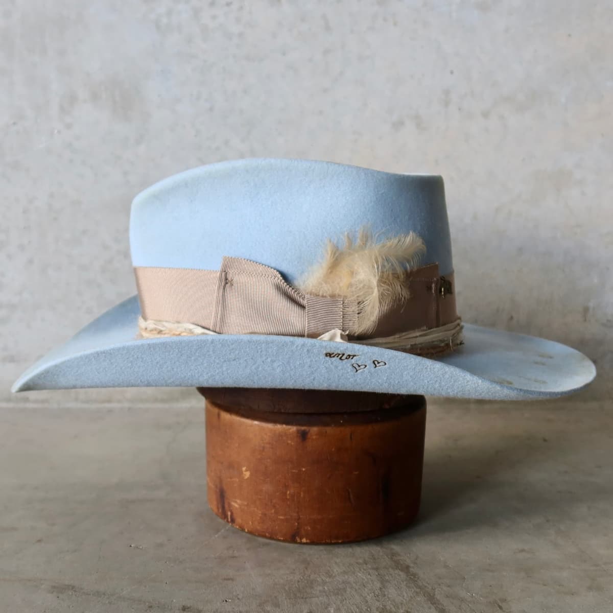 Left side view of the Crystal Blue felt cowboy hat Clareville Limited Edition by PHYLLi Designs with natural sari silk trim, twine wraps and bronze pearl and leaf charm.