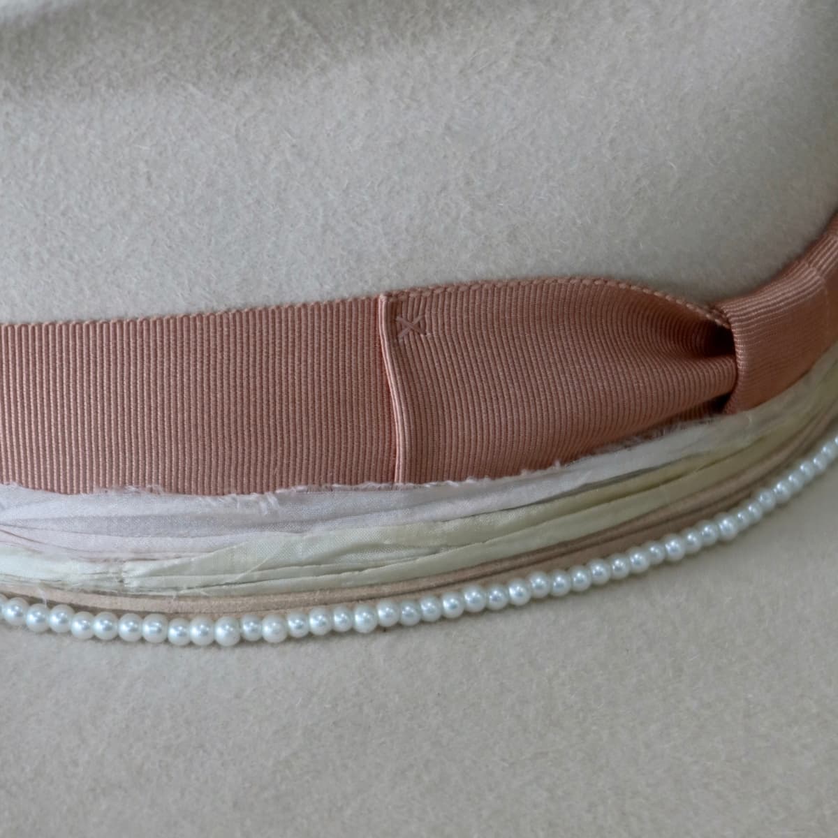 Close up detail of the Clementine felt hat showing dirty rose grosgrain brim trim and pearl necklace detail.