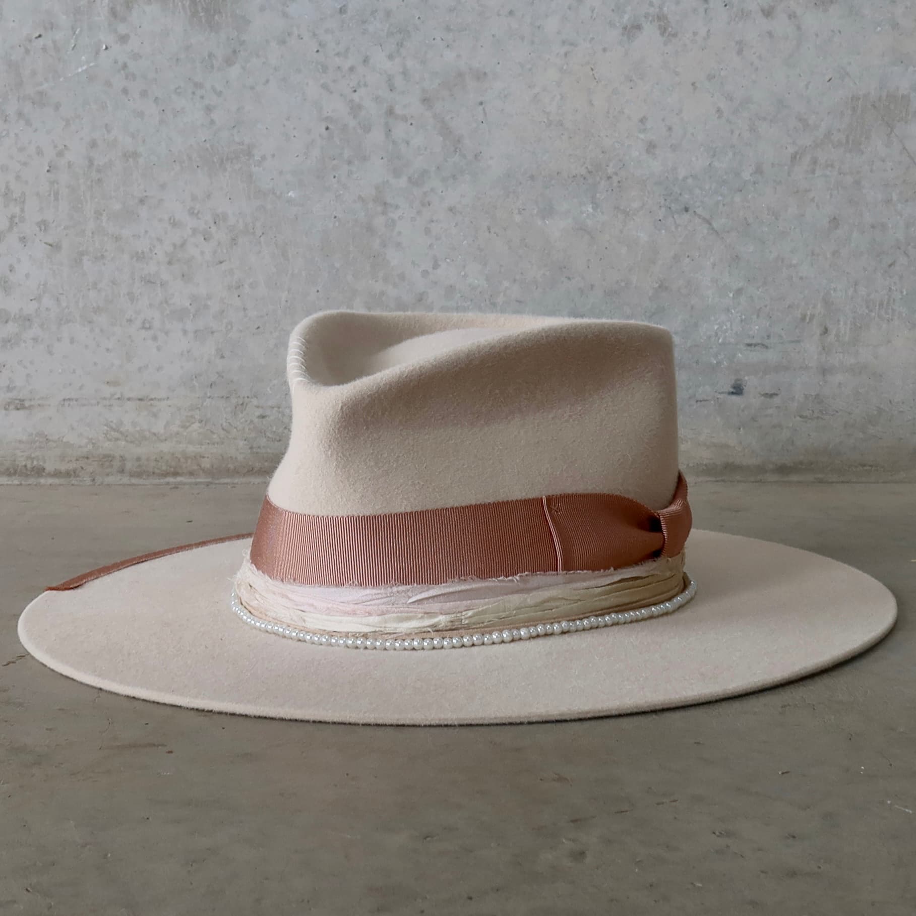 Front left angle of the beige felt hat Clementine by PHYLLi Designs with dirty rose grosgrain band, sari silk trim and pearl hat necklace.