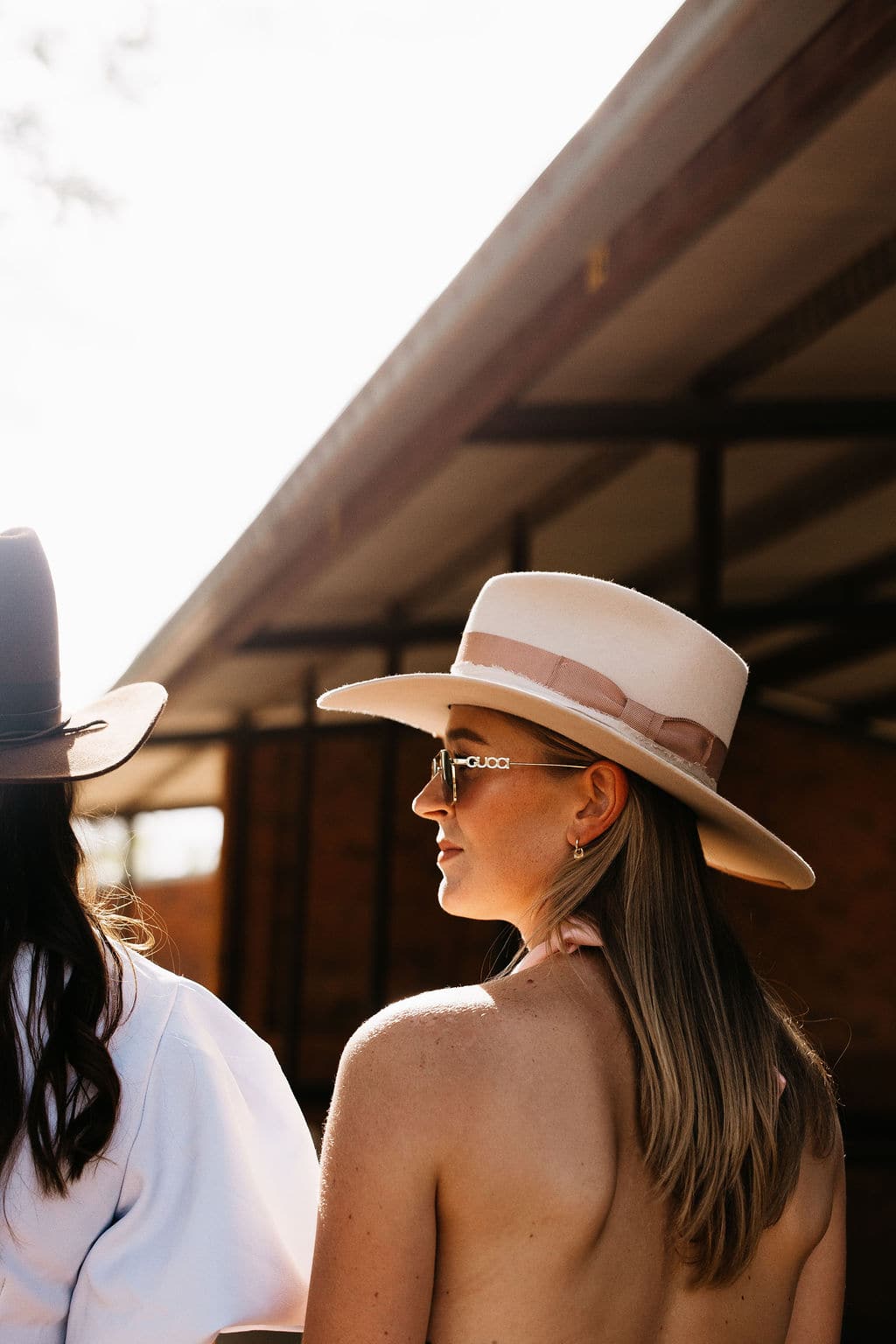 Side profile of a woman wearing the PHYLLi Clementine, a beige wide brim felt hat with a pearl hat necklace, outdoors.