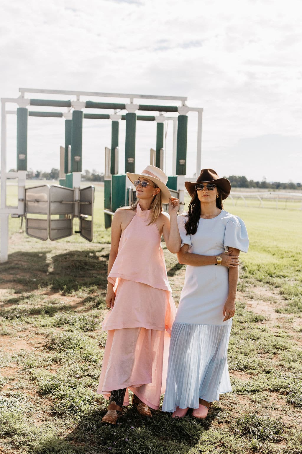 Woman in the PHYLLi Clementine beige felt hat standing with a friend on a racetrack beside white starting gate.