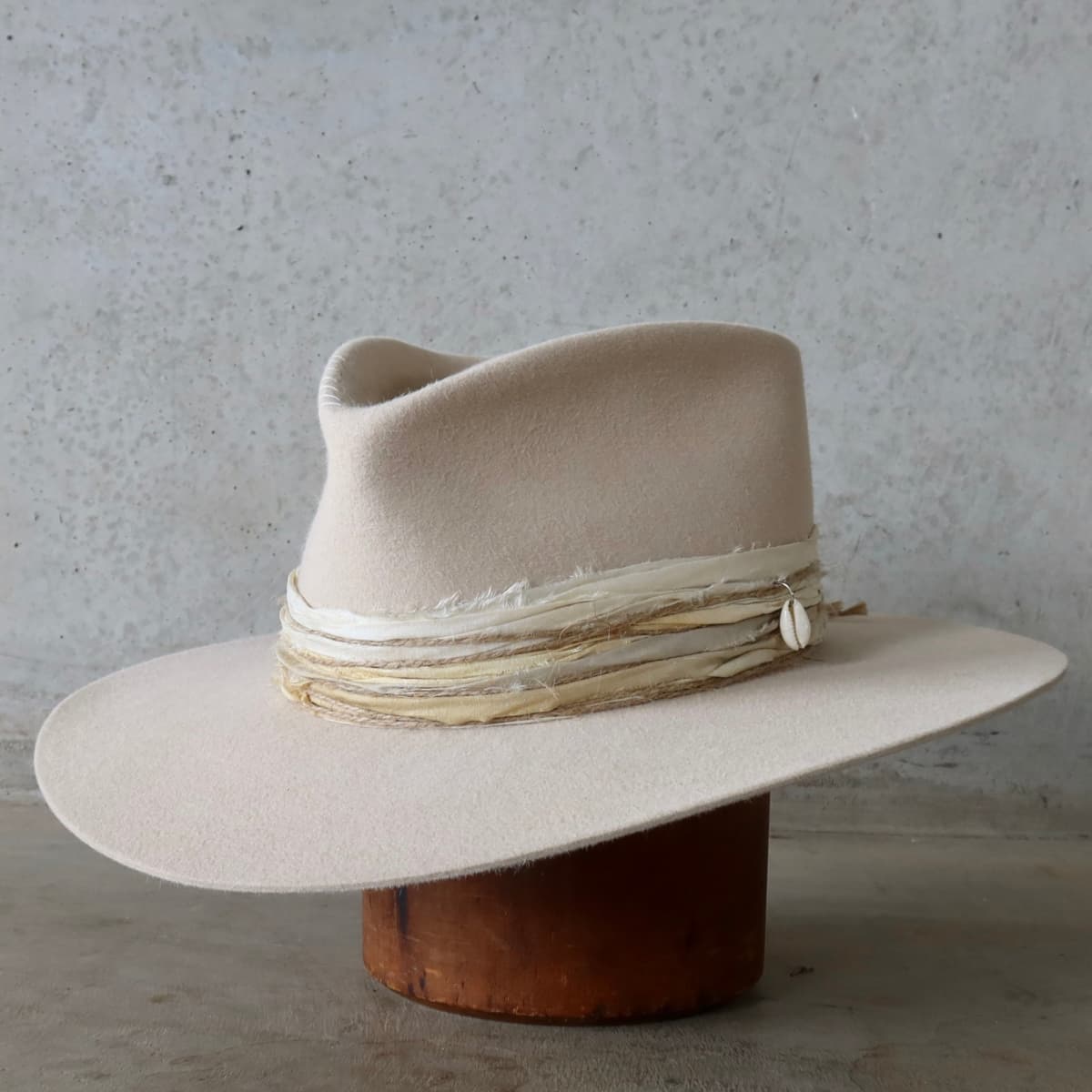 Front left angle of the beige felt hat Coastline by PHYLLi Designs with ivory grosgrain band, sand and blue tie-dye sari silk trim and twine wraps.