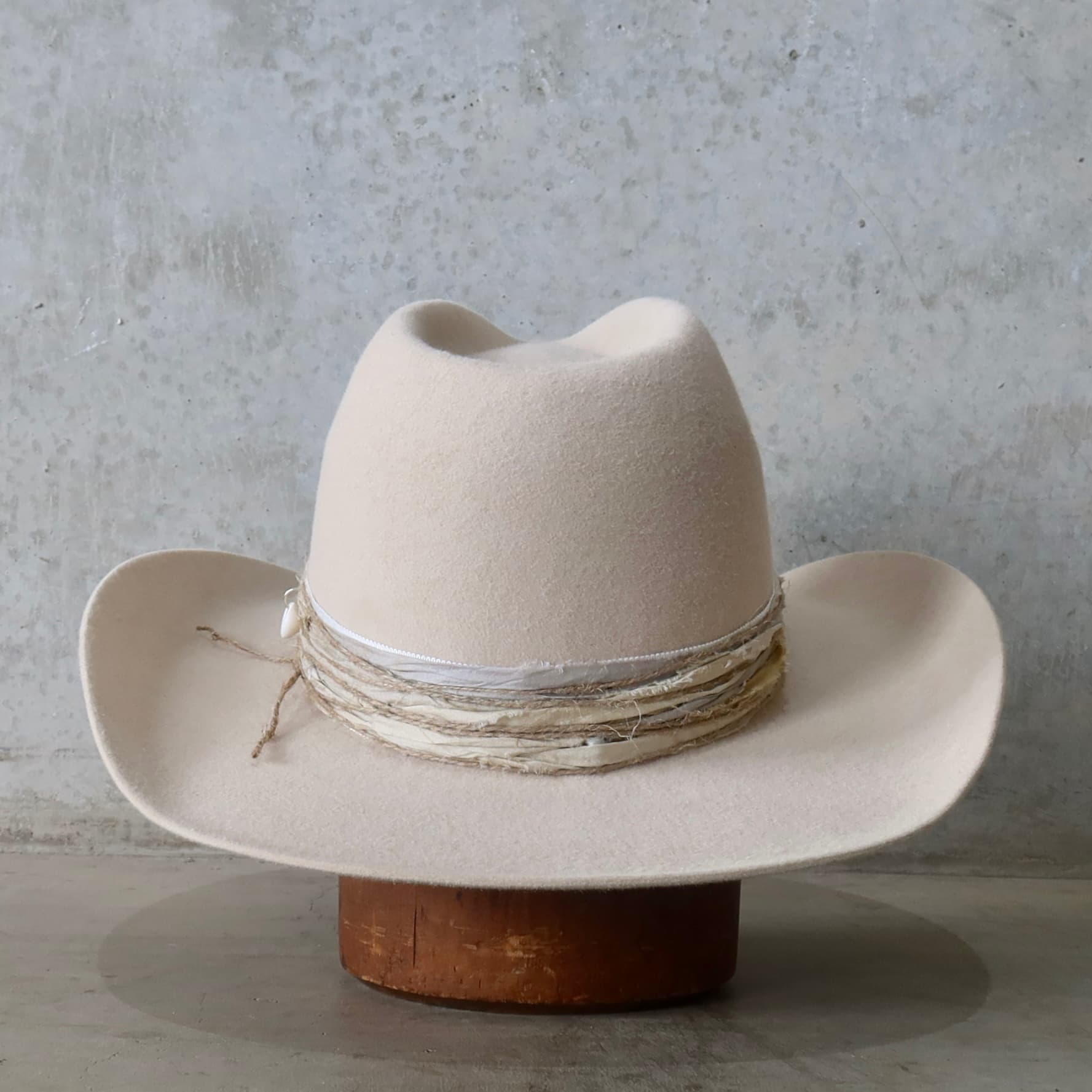 Back view of the beige felt cowboy hat Coastline Cowgirl by PHYLLi Designs featuring twine wraps and cowrie shell charm.