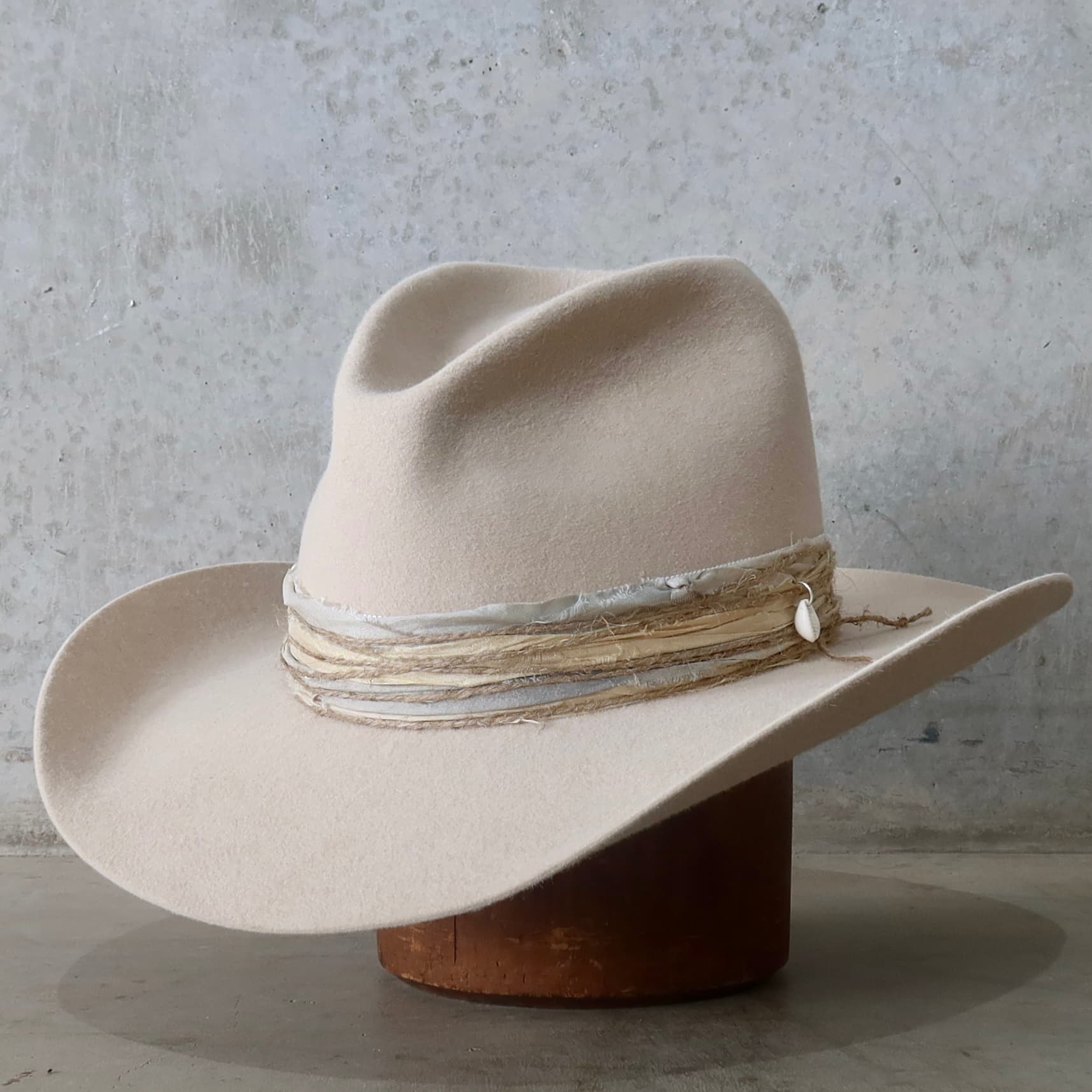 Front left angle of the beige felt cowboy hat Coastline Cowgirl by PHYLLi Designs with sand and blue tie-dye sari silk trim and twine wraps.