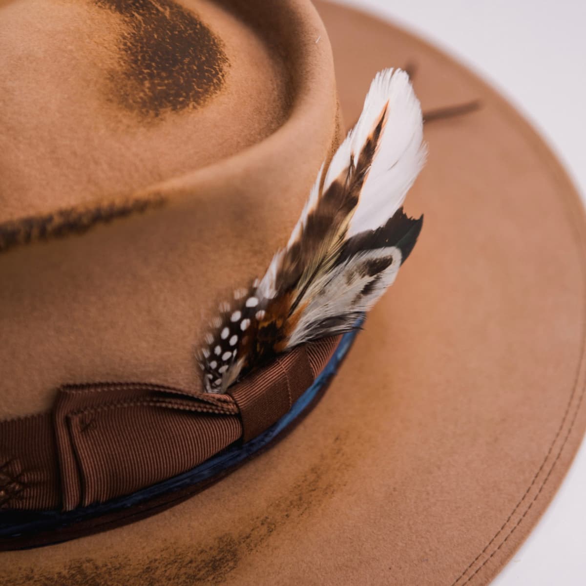 Close up detail of the Columbian felt hat showing the feather bunch set into the distressed chocolate grosgrain bow band.
