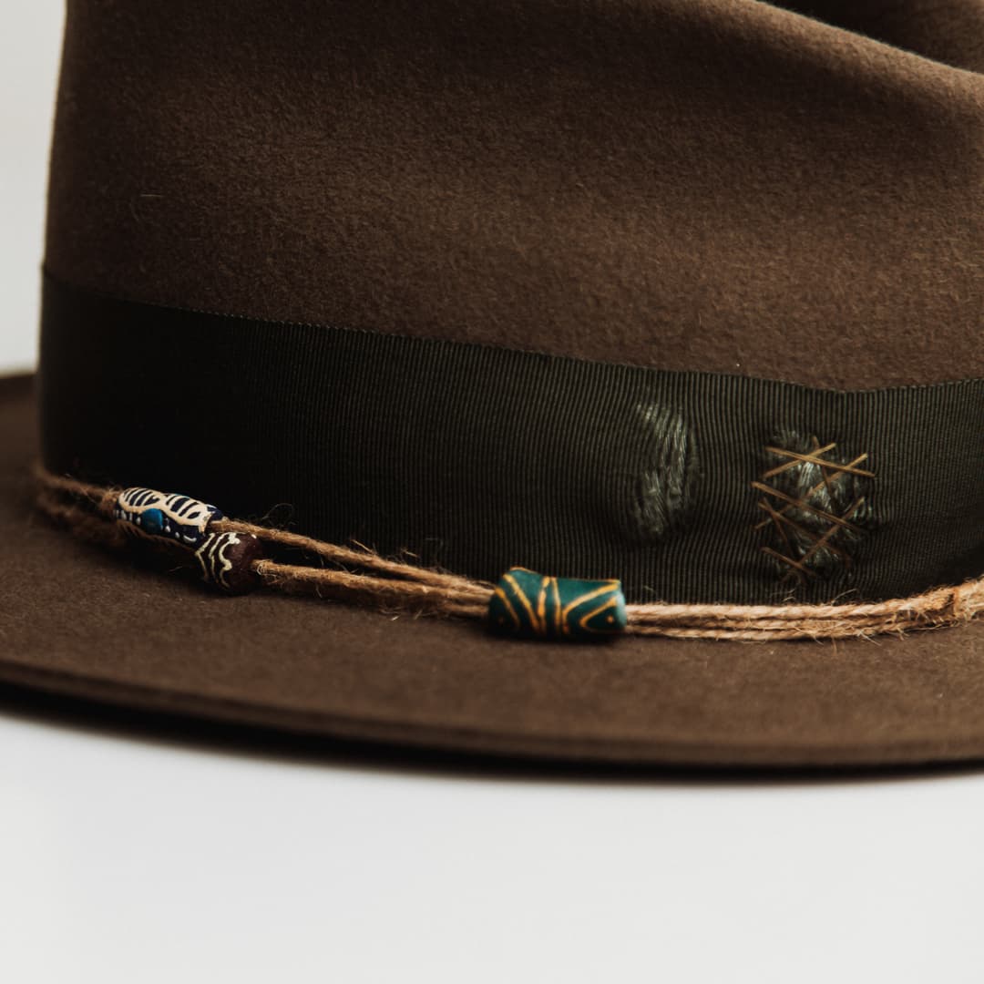 Close up detail of the Congo felt hat showing hand painted recycled glass bead from Ghana on twine wrap.