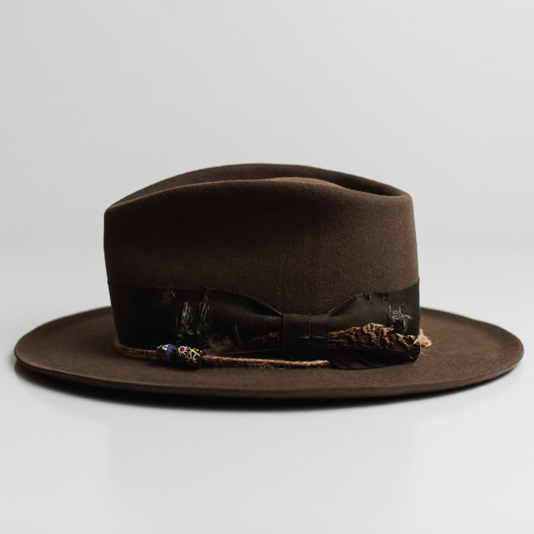 Left side view of the Congo dirty olive felt hat by PHYLLi Designs with distressed artichoke grosgrain band, moss darned patch and twine wrap with bead.
