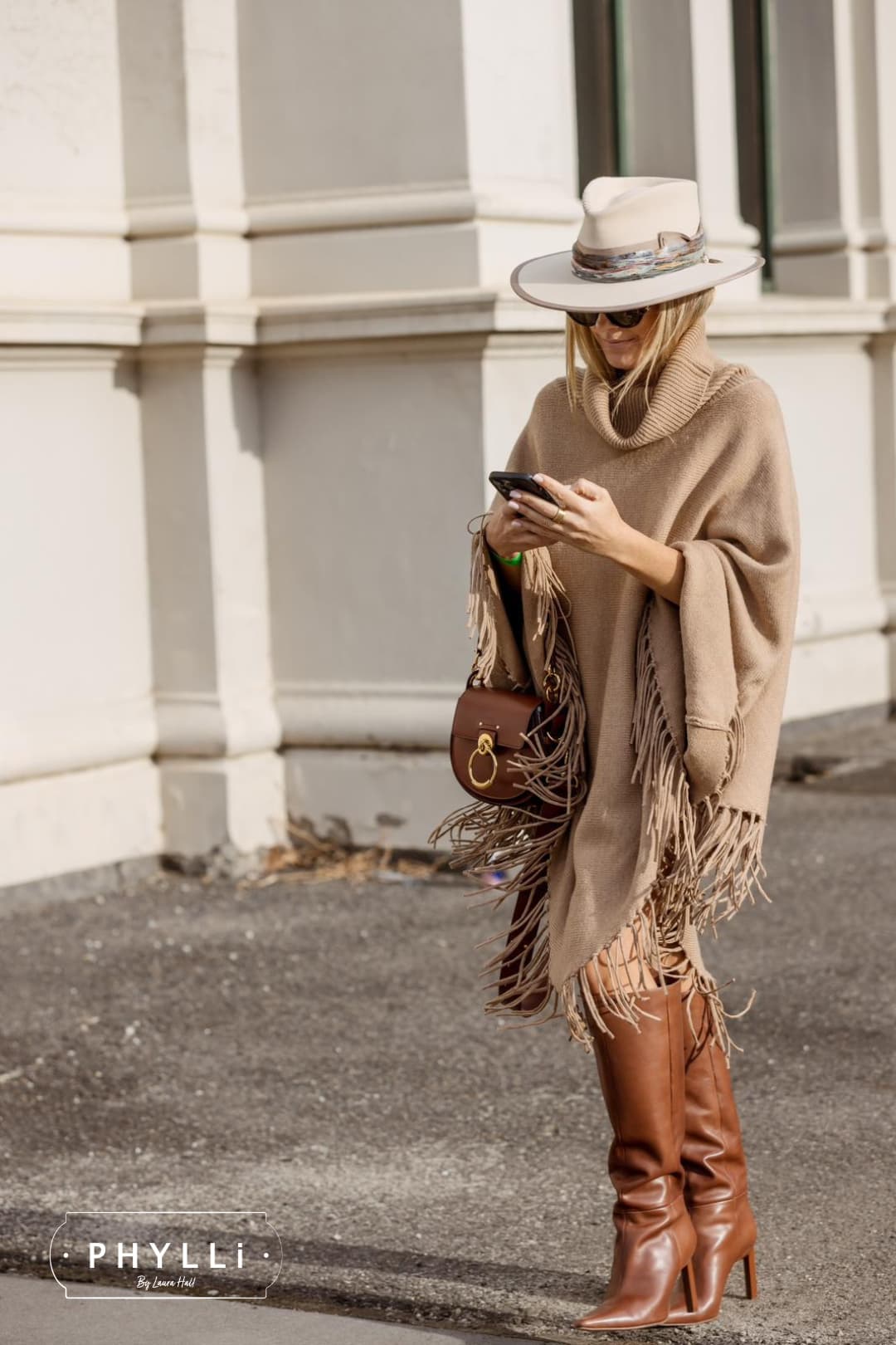 Woman wearing the Cunningham beige felt hat by PHYLLi Designs with jewel toned sari silk trim and bronze charm cluster while walking along a city street.