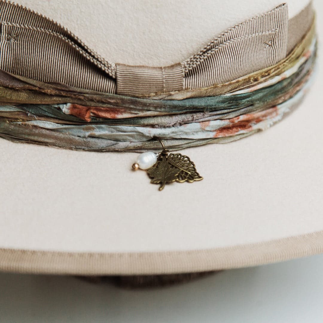 Close up detail of the Cunningham felt hat showing bronze leaf charms and pearl pendant attached to the sari silk trim.
