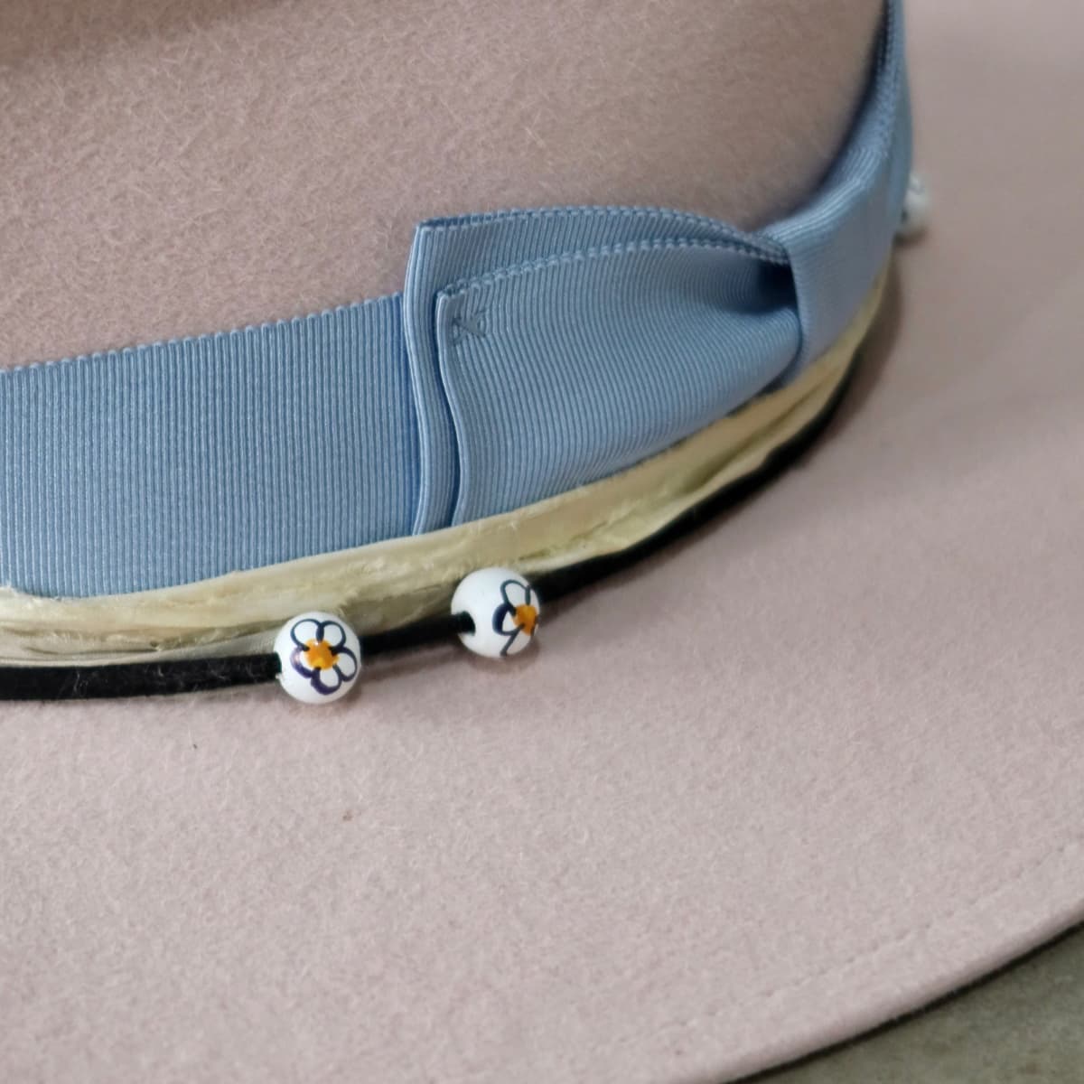 Close up detail of the Daisy felt hat showing hand-painted timber daisy beads on black suede string.