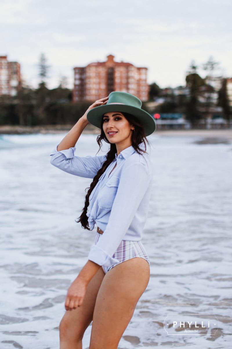 Woman walking on the beach wearing the Diamonds & Pearls eucalyptus felt hat by PHYLLi Designs with pearl charm hat pin and cream candy patterned sari silk trim.