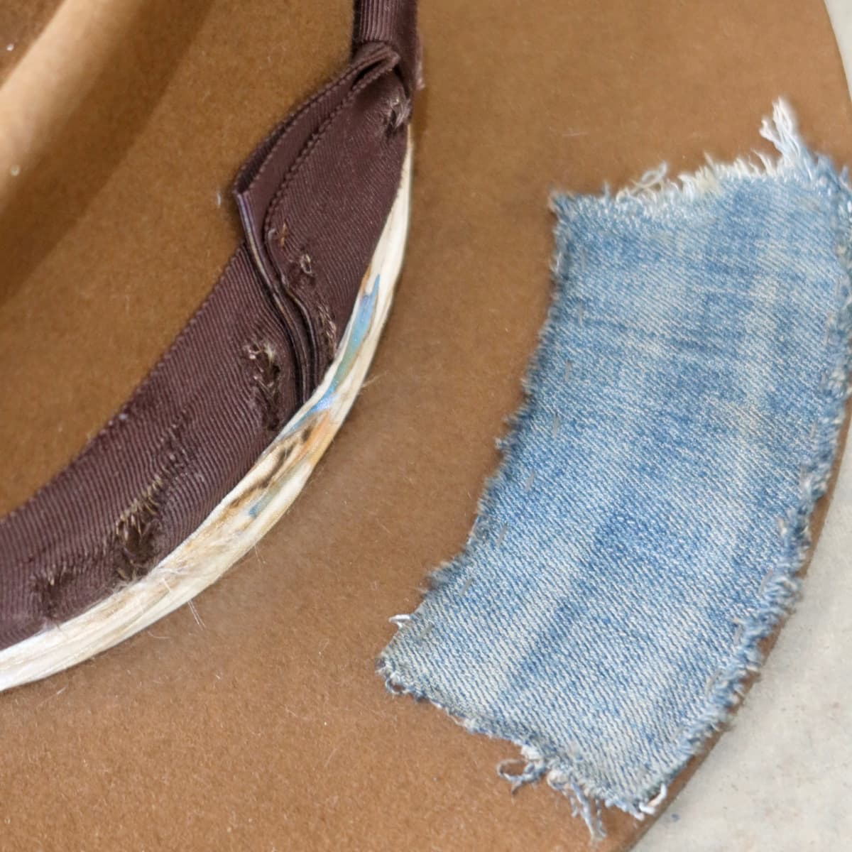 Close up detail of the Duke Limited Edition felt hat showing distressed chocolate grosgrain band and worn denim patch trim.