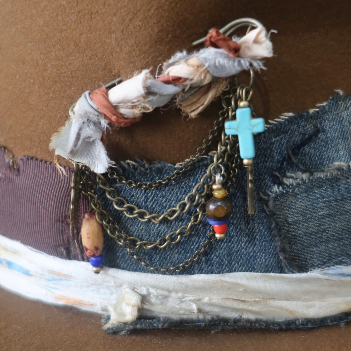 Close up detail of the Duke Limited Edition felt hat showing bronze chunky hat pin with sari silk, charms and beads.