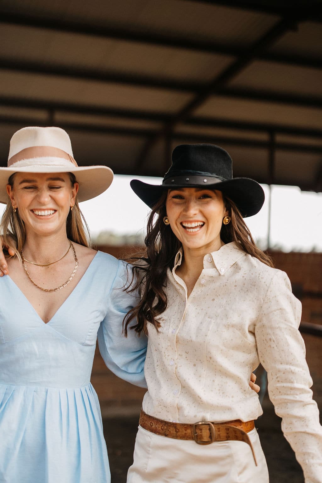Woman wearing the PHYLLi Edwards black felt cowboy hat, standing beside a model wearing the Clementine beige hat in a rural setting.