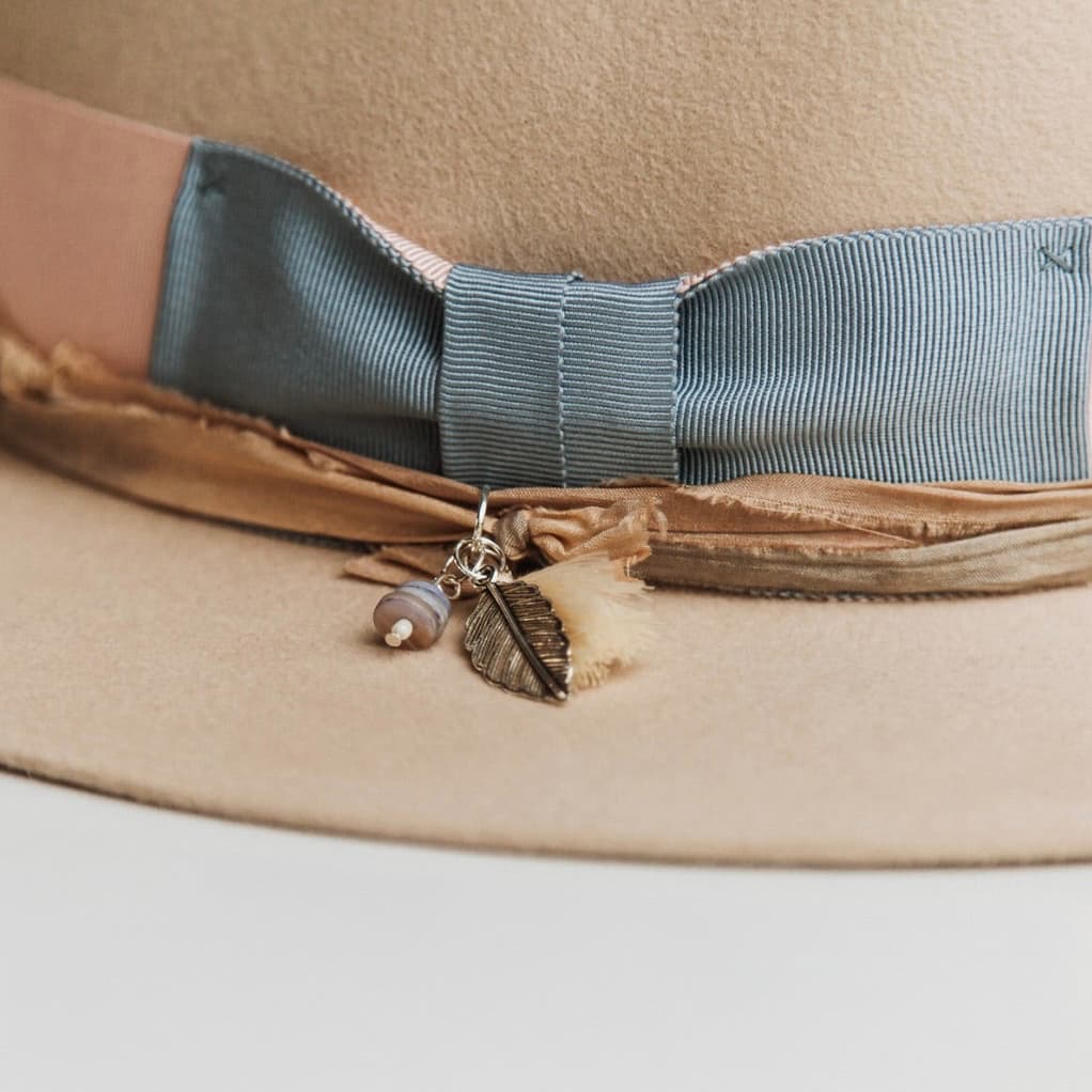 Close up detail of the Eleanor felt hat showing cornflower grosgrain bow and charm cluster with silver charm and bead.